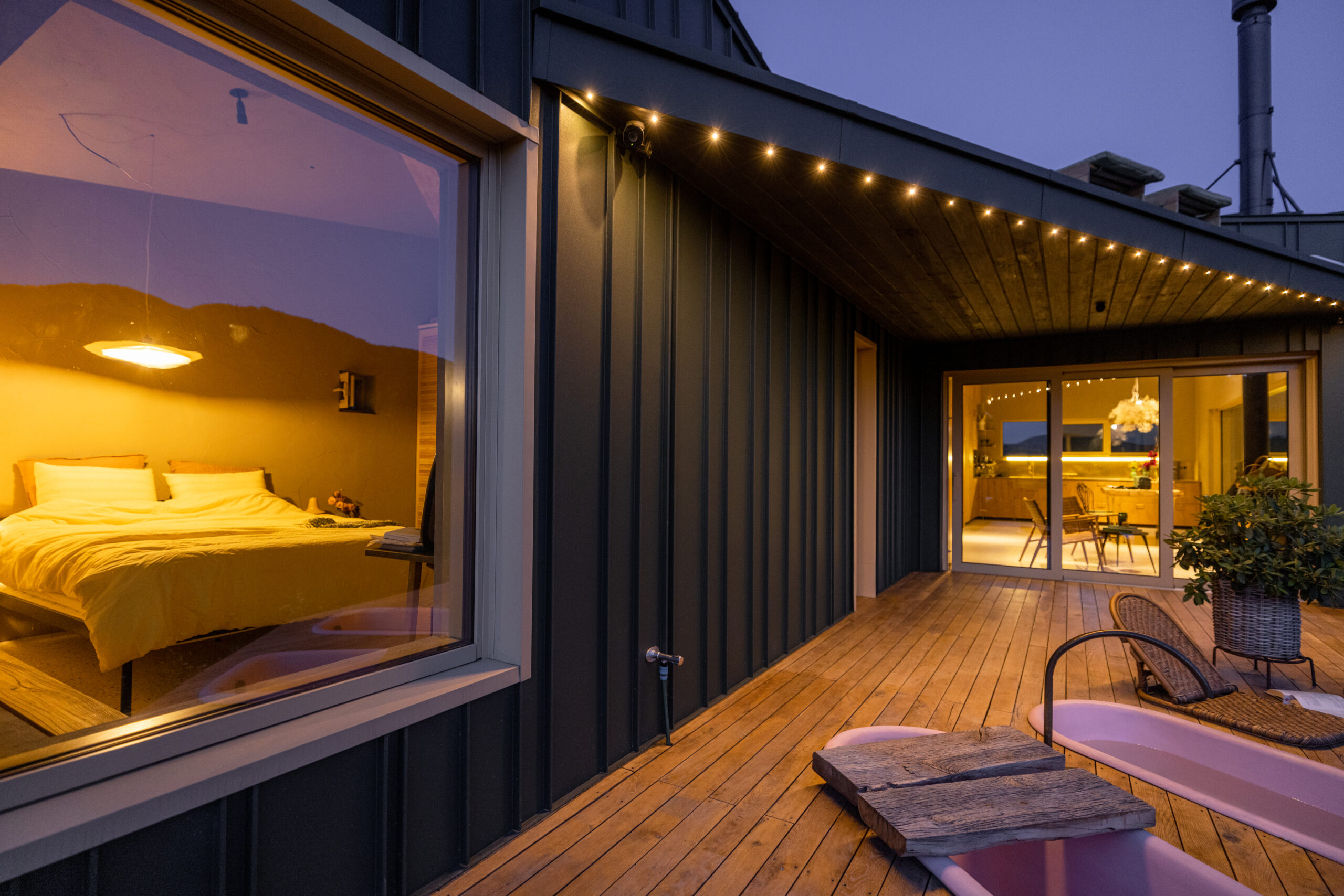 Evening glow from a cozy bedroom window with a pet dog looking outside. The wooden deck leads to an inviting interior illuminated by soft, ambient lights